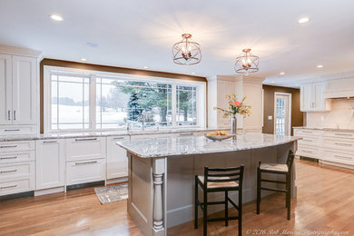 Example of a large transitional l-shaped light wood floor and beige floor enclosed kitchen design in Boston with shaker cabinets, white cabinets, granite countertops, white backsplash, ceramic backsplash, an island, an undermount sink, stainless steel appliances and multicolored countertops