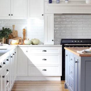 Large country u-shaped open plan kitchen in Melbourne with an undermount sink, shaker cabinets, white cabinets, quartz benchtops, white splashback, subway tile splashback, black appliances, medium hardwood floors, with island, white benchtop and beige floor.