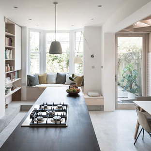 Medium sized contemporary galley kitchen/diner in London with flat-panel cabinets, white cabinets, concrete flooring, an island, grey floors and black worktops.