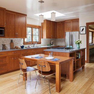 Cette image montre une cuisine américaine craftsman en L de taille moyenne avec un placard à porte shaker, des portes de placard en bois brun, un électroménager en acier inoxydable, un îlot central, un plan de travail en quartz modifié, une crédence beige, une crédence en carreau de céramique, un sol en bambou et un sol beige.