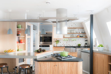 This is an example of a contemporary u-shaped open plan kitchen in London with a belfast sink, flat-panel cabinets, light wood cabinets, concrete worktops, white splashback, stainless steel appliances and a breakfast bar.