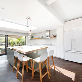 Photo of a large contemporary single-wall open plan kitchen in London with a belfast sink, flat-panel cabinets, white cabinets, quartz worktops, white splashback, matchstick tiled splashback, black appliances, dark hardwood flooring, an island, brown floors and white worktops.
