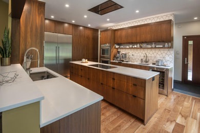 Example of a 1950s u-shaped medium tone wood floor and brown floor kitchen design in Boston with an undermount sink, flat-panel cabinets, medium tone wood cabinets, white backsplash, stainless steel appliances and white countertops