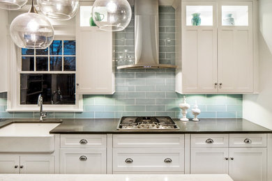 Design ideas for a large traditional galley enclosed kitchen in Omaha with a submerged sink, shaker cabinets, white cabinets, engineered stone countertops, blue splashback, glass tiled splashback, stainless steel appliances, medium hardwood flooring, an island and brown floors.
