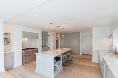This is an example of a large classic galley kitchen in Other with recessed-panel cabinets, white cabinets, marble worktops, white splashback, stainless steel appliances, light hardwood flooring and an island.