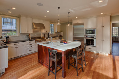 Inspiration for a mid-sized craftsman u-shaped medium tone wood floor eat-in kitchen remodel in Boston with an undermount sink, shaker cabinets, white cabinets, marble countertops, white backsplash, stainless steel appliances and an island