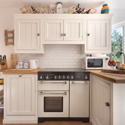 Inspiration for a small timeless l-shaped medium tone wood floor kitchen remodel in Devon with recessed-panel cabinets, white cabinets, wood countertops, white backsplash, white appliances, a peninsula and subway tile backsplash