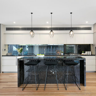 Inspiration for a mid-sized contemporary l-shaped kitchen in Sydney with window splashback, stainless steel appliances, medium hardwood floors, with island, black benchtop, flat-panel cabinets, white cabinets, an undermount sink, beige floor and marble benchtops.