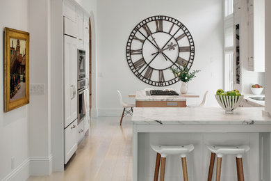 Exempel på ett medelhavsstil vit vitt kök, med vita skåp, ljust trägolv, beiget golv, marmorbänkskiva, integrerade vitvaror och en halv köksö