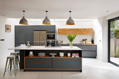 Cette photo montre une cuisine parallèle tendance avec un placard à porte plane, des portes de placard grises, une crédence blanche, un électroménager en acier inoxydable et îlot.