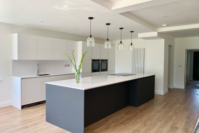 Inspiration for a large contemporary galley open plan kitchen in Cheshire with flat-panel cabinets, grey cabinets, quartz worktops, white splashback, stainless steel appliances, laminate floors, an island and white worktops.