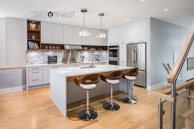 Example of a small minimalist l-shaped light wood floor open concept kitchen design in Ottawa with an undermount sink, flat-panel cabinets, white cabinets, quartz countertops, gray backsplash, stone tile backsplash, stainless steel appliances and an island