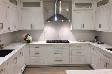 Mid-sized transitional u-shaped medium tone wood floor and brown floor enclosed kitchen photo in New York with a peninsula, an undermount sink, shaker cabinets, white cabinets, marble countertops, white backsplash, stainless steel appliances and marble backsplash