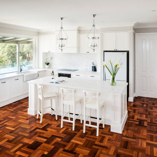 This is an example of a large traditional l-shaped eat-in kitchen in Melbourne with shaker cabinets, with island, a farmhouse sink, white cabinets, quartz benchtops, black appliances and dark hardwood floors.
