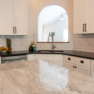 Modern kitchen designs - Inspiration for a modern beige floor kitchen remodel in Raleigh with white cabinets, white backsplash, ceramic backsplash, stainless steel appliances, an island and black countertops