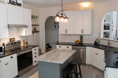 Example of a minimalist beige floor kitchen design in Raleigh with white cabinets, white backsplash, ceramic backsplash, stainless steel appliances, an island and black countertops