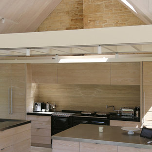 Photo of a medium sized contemporary galley kitchen/diner in Gloucestershire with flat-panel cabinets, stainless steel worktops, beige splashback, multiple islands, black worktops, light wood cabinets, integrated appliances and grey floors.
