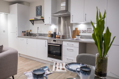 This is an example of a medium sized modern galley kitchen/diner in Surrey with a double-bowl sink, flat-panel cabinets, white cabinets, laminate countertops, grey splashback, stainless steel appliances, no island and grey worktops.