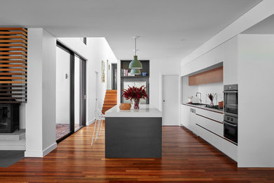 Idéer för att renovera ett funkis vit vitt l-kök, med bänkskiva i kvarts, vitt stänkskydd, en köksö, släta luckor, vita skåp, rostfria vitvaror, mörkt trägolv och brunt golv