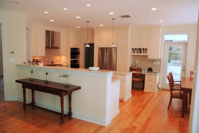 Inspiration for a mid-sized timeless u-shaped light wood floor and beige floor open concept kitchen remodel in DC Metro with a double-bowl sink, raised-panel cabinets, white cabinets, granite countertops, brown backsplash, glass tile backsplash, stainless steel appliances and a peninsula