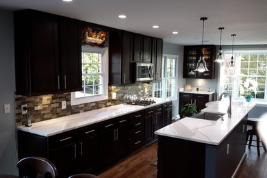 Large classic u-shaped kitchen/diner in DC Metro with a belfast sink, shaker cabinets, dark wood cabinets, engineered stone countertops, brown splashback, glass tiled splashback, stainless steel appliances, medium hardwood flooring, an island, brown floors and white worktops.