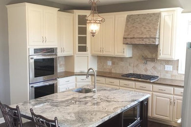 Example of a small trendy l-shaped dark wood floor and brown floor enclosed kitchen design in Chicago with granite countertops, beige backsplash, travertine backsplash, paneled appliances, an island, an undermount sink, raised-panel cabinets and white cabinets