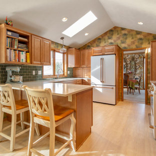 This is an example of a transitional u-shaped kitchen in Seattle with an undermount sink, raised-panel cabinets, medium wood cabinets, green splashback, subway tile splashback, white appliances, light hardwood floors, a peninsula, beige floor, beige benchtop and vaulted.