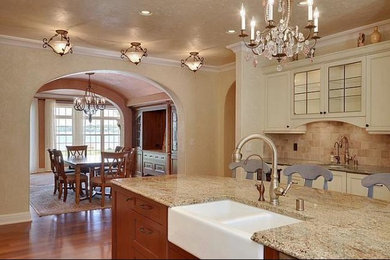Inredning av ett klassiskt stort kök, med en rustik diskho, luckor med infälld panel, vita skåp, granitbänkskiva, beige stänkskydd, stänkskydd i stenkakel, ljust trägolv, en köksö och brunt golv