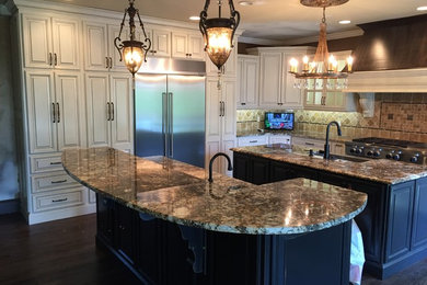 Large transitional l-shaped dark wood floor kitchen photo in Atlanta with a farmhouse sink, raised-panel cabinets, white cabinets, granite countertops, beige backsplash, stone tile backsplash, stainless steel appliances and two islands