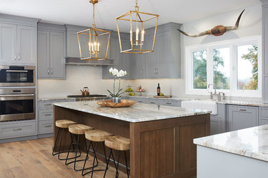 Eat-in kitchen - large u-shaped medium tone wood floor eat-in kitchen idea in Grand Rapids with a farmhouse sink, beaded inset cabinets, gray cabinets, granite countertops, gray backsplash, ceramic backsplash, paneled appliances and an island