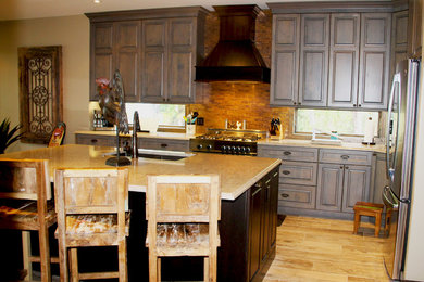 Photo of a large classic l-shaped enclosed kitchen in Miami with a submerged sink, raised-panel cabinets, brown cabinets, engineered stone countertops, brown splashback, mosaic tiled splashback, stainless steel appliances, light hardwood flooring, an island, brown floors and beige worktops.