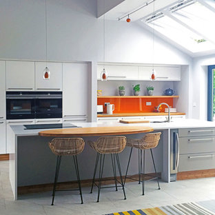 This is an example of a large modern open plan kitchen in Other with an integrated sink, flat-panel cabinets, orange splashback, glass sheet splashback, black appliances and with island.