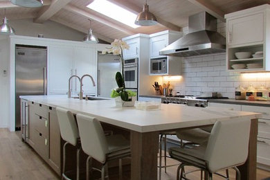 Example of a mid-sized cottage l-shaped medium tone wood floor and brown floor enclosed kitchen design in Los Angeles with an undermount sink, shaker cabinets, white cabinets, marble countertops, white backsplash, subway tile backsplash, stainless steel appliances, an island and white countertops