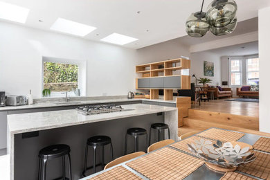 Photo of a large modern galley open plan kitchen in Sussex with an integrated sink, flat-panel cabinets, grey cabinets, granite worktops, multi-coloured splashback, granite splashback, stainless steel appliances, porcelain flooring, a breakfast bar, grey floors, multicoloured worktops and a drop ceiling.