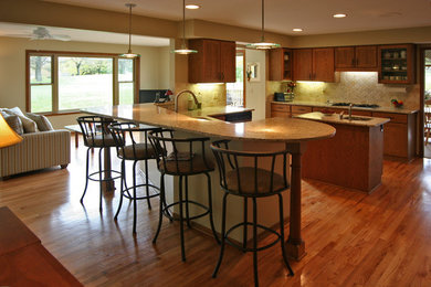 Eat-in kitchen - mid-sized traditional l-shaped medium tone wood floor eat-in kitchen idea in Detroit with an undermount sink, shaker cabinets, medium tone wood cabinets, granite countertops, beige backsplash, stone tile backsplash, stainless steel appliances and an island