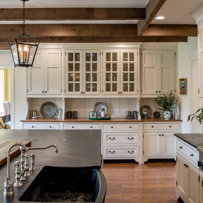 Huge elegant u-shaped medium tone wood floor and brown floor enclosed kitchen photo in Philadelphia with a farmhouse sink, beaded inset cabinets, beige cabinets, soapstone countertops, beige backsplash, wood backsplash, stainless steel appliances, an island and black countertops