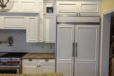 Elegant kitchen photo in Salt Lake City with raised-panel cabinets, white cabinets, granite countertops, white backsplash, ceramic backsplash, paneled appliances and an island