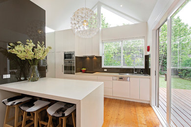 Exempel på ett mellanstort modernt kök, med släta luckor, vita skåp, grått stänkskydd, en köksö, en nedsänkt diskho, bänkskiva i kvarts, stänkskydd i sten, rostfria vitvaror och ljust trägolv
