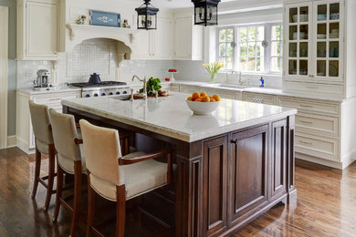 Bild på ett stort vintage kök, med en undermonterad diskho, luckor med profilerade fronter, vita skåp, vitt stänkskydd, stänkskydd i porslinskakel, integrerade vitvaror, mellanmörkt trägolv, en köksö, brunt golv och marmorbänkskiva