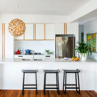 Immagine di un cucina con isola centrale contemporaneo con ante lisce, ante bianche, paraspruzzi bianco e elettrodomestici in acciaio inossidabile