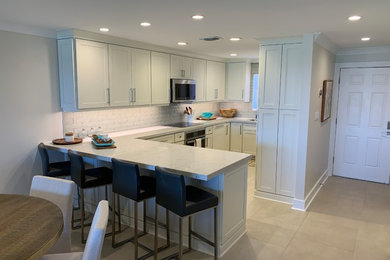 Example of a mid-sized beach style l-shaped porcelain tile and gray floor eat-in kitchen design in Miami with an undermount sink, recessed-panel cabinets, blue cabinets, quartzite countertops, gray backsplash, ceramic backsplash, stainless steel appliances, a peninsula and white countertops