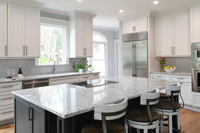 Example of a mid-sized beach style l-shaped brown floor eat-in kitchen design in Charleston with an undermount sink, flat-panel cabinets, white cabinets, solid surface countertops, white backsplash, porcelain backsplash, stainless steel appliances, an island and multicolored countertops