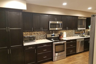Inspiration for a large transitional l-shaped medium tone wood floor eat-in kitchen remodel in Milwaukee with an undermount sink, shaker cabinets, dark wood cabinets, granite countertops, brown backsplash, glass tile backsplash and stainless steel appliances