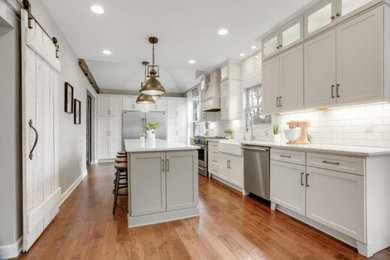 Inspiration for a large country u-shaped dark wood floor, brown floor and vaulted ceiling eat-in kitchen remodel in Columbus with a farmhouse sink, shaker cabinets, white cabinets, quartz countertops, white backsplash, porcelain backsplash, stainless steel appliances, an island and white countertops