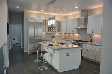 Mid-sized trendy l-shaped dark wood floor and brown floor enclosed kitchen photo in Portland with an undermount sink, shaker cabinets, white cabinets, solid surface countertops, white backsplash, subway tile backsplash, stainless steel appliances and an island