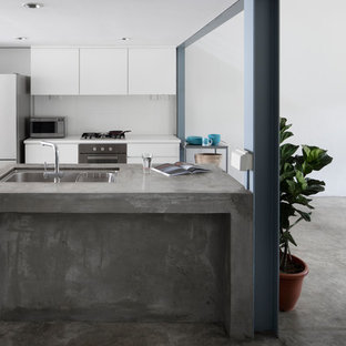 Inspiration for an industrial galley kitchen in Singapore with a drop-in sink, flat-panel cabinets, white cabinets, concrete benchtops, white splashback, white appliances, concrete floors, multiple islands, grey floor and grey benchtop.
