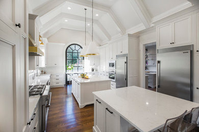 Design ideas for a traditional u-shaped enclosed kitchen in Nashville with a belfast sink, recessed-panel cabinets, white cabinets, stainless steel appliances, medium hardwood flooring, multiple islands, quartz worktops and brown floors.