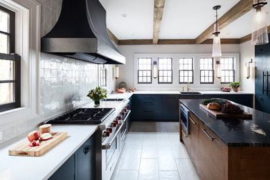 Traditional u-shaped kitchen in New York with a belfast sink, flat-panel cabinets, blue cabinets, white splashback, stainless steel appliances, an island, grey floors and white worktops.