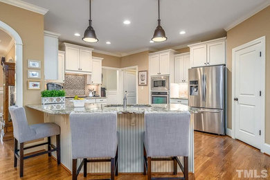 Inspiration for a mid-sized transitional u-shaped medium tone wood floor and brown floor kitchen remodel in Raleigh with white cabinets, stainless steel appliances, no island, multicolored countertops, recessed-panel cabinets, granite countertops, an undermount sink, beige backsplash and travertine backsplash
