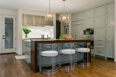 Open concept kitchen - large transitional l-shaped medium tone wood floor open concept kitchen idea in Austin with a farmhouse sink, recessed-panel cabinets, green cabinets, marble countertops, white backsplash, stone slab backsplash, paneled appliances and an island